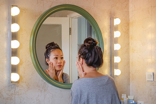 A woman looks in the mirror with concerns about unwanted hair growth