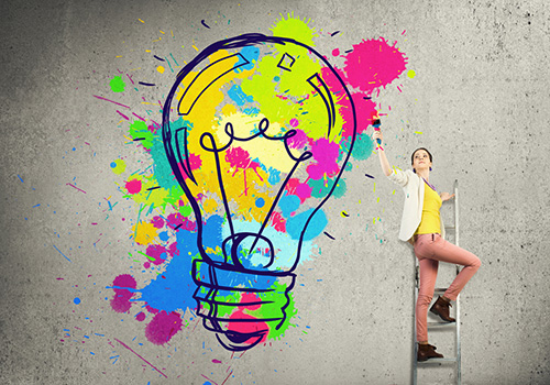 woman on ladder creating a big colorful lightbulb as an idea
