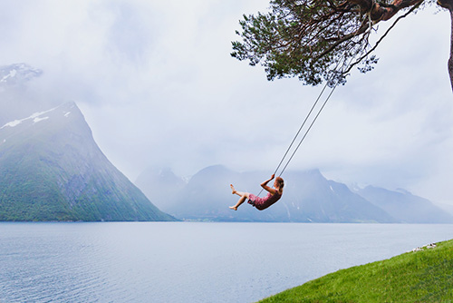 woman swinging in beautiful daydream setting of water and mountains
